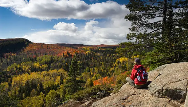 Female hiker sitting on rocky ledge taking in a scenic Autumn view in Minnesota's Arrowhead region from Oberg Mountain.