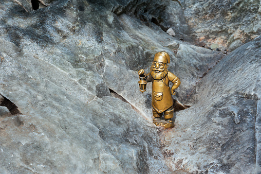 A small bronze gnome sculpture for good luck, standing on granite, holds a lamp.