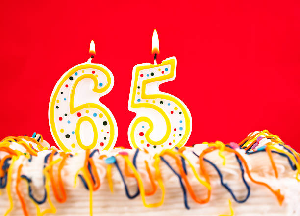 istock Decorated birthday cake with number 65 burning candles. Red background. 182473551