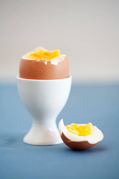 Cracked hard boiled brown egg in a white egg cup stock photo