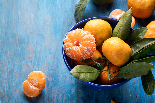 Fresh juicy tangerines in blue ceramic bowl on wooden background.