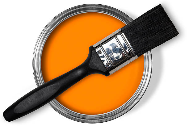 Paint brush sitting on tin of bright orange paint stock photo