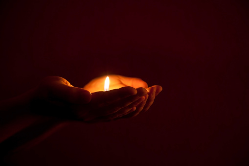 burning candle in human hands in darkness