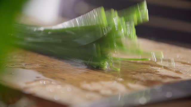 Wet Chopped Green Chives Falling onto Wooden Cutting Board
