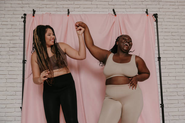 istock Two playful plus size African women in underwear holding hands while standing on fabric background 1824781049