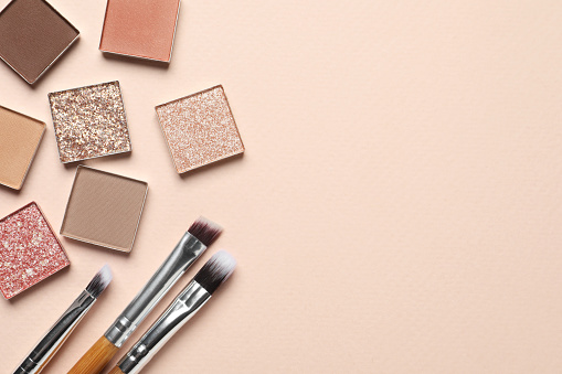 Different beautiful eye shadows and makeup brushes on beige background, flat lay. Space for text