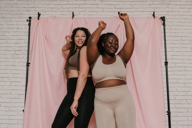istock Two smiling plus size African women in sportswear dancing while standing on fabric background together 1824781066