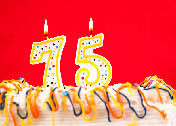 istock Decorated birthday cake with number 75 burning candles. Red background. 182478917