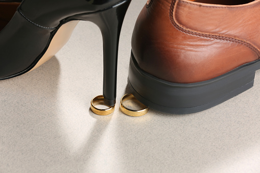 Woman's heel and man's shoe stepped on gold wedding rings against light gray background, closeup. Divorce concept