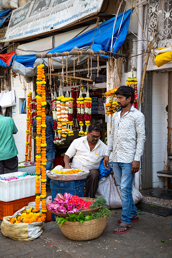 22nd January, 2020 - Mumbai, India: This editorial image captures the lively and colourful atmosphere of a flower market in Mumbai, bustling with activity. The market is a sensory delight, filled with various flowers' vibrant hues and fragrances, from marigolds and roses to jasmine and lotuses. The people in the photograph, comprising of both sellers and local buyers, are engaged in the vibrant trade that characterises this market. Sellers are seen arranging their floral wares creating eye-catching displays, while locals browse and select flowers for various purposes, from religious rituals to personal and home decoration. The image aims to depict the integral role of the flower market in Mumbai's daily life, highlighting the cultural significance of flowers in India and the market's place as a hub of commerce and community interaction.
