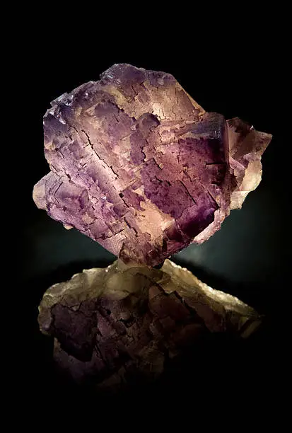 "Rough purple and white Fluorite crystals lit from behind, on a reflective surface."