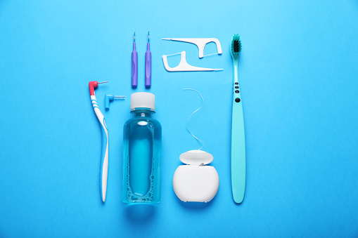 Dental floss and different teeth care products on light blue background, flat lay