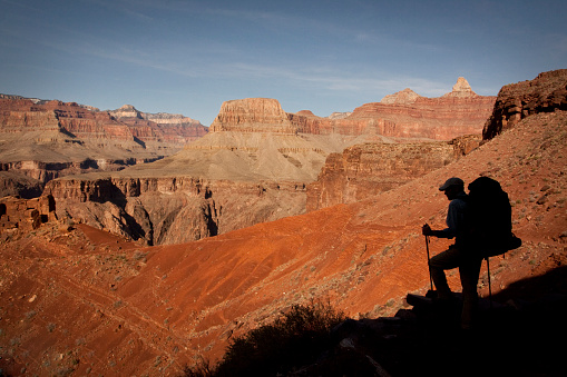 Silhouetted hiker against the Grand Canyon under blue skies. 