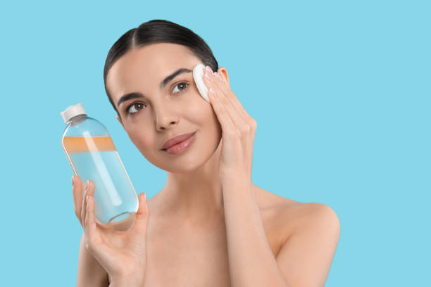 istock Beautiful woman removing makeup with cotton pad on light blue background, space for text 1824865426