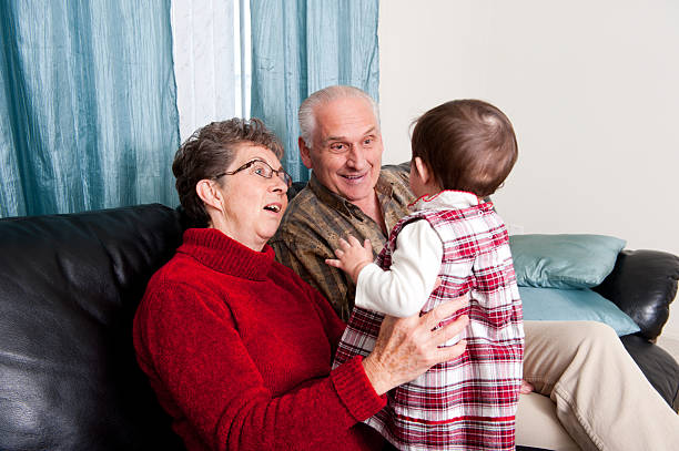Grandmother holds grandson on her lap sitting on a sofa. Baby wearing a Santa Claus costume.