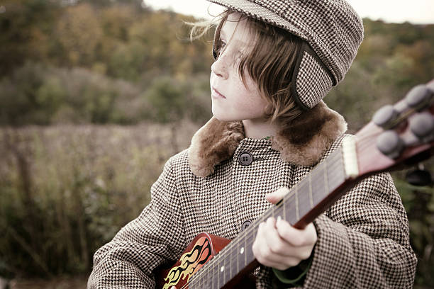 Adorable Little Boy Playing Guitar at Prairie- Vintage Toning "Adorable little boy in vintage hat and jacket plays red guitar at the prairie. Toned in a golden vintage process.Shot with Canon 1Ds Mark II, cross processed and color saturation reduced, golden toned, vignette added, copy space." rockabilly boys stock pictures, royalty-free photos & images