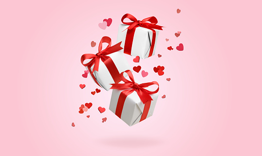 White gift boxes with red bows flying with hearts and falling on pink background. Valentine's Day background, greeting Card. February 14th. Copy space.
