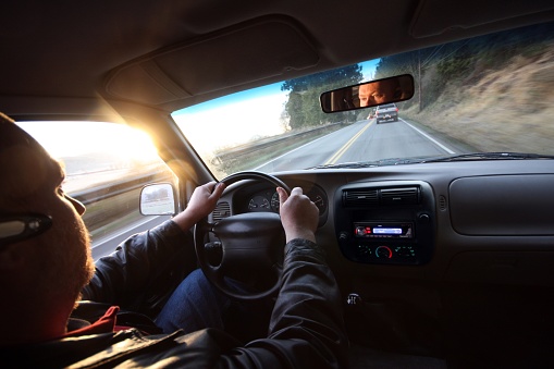 Over the shoulder view of a middle-aged man driving an SUV (morning comute) while talking on a hands-free cell-phone.