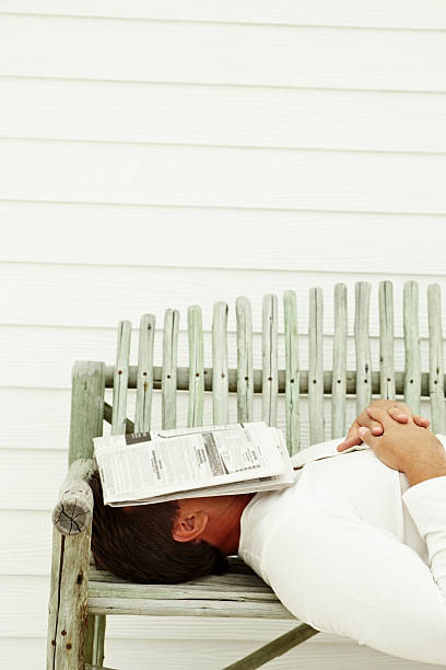 Mature guy taking a nap on bench with newspaper on face