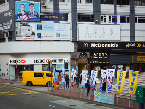 People waiting across the road with a HSBC bank and McDonald's as background. , Tai Koo, Hong Kong. November 25 2023. With long shot, wide angle lens, high angle. Day, exterior, sunny, winter, dry season.