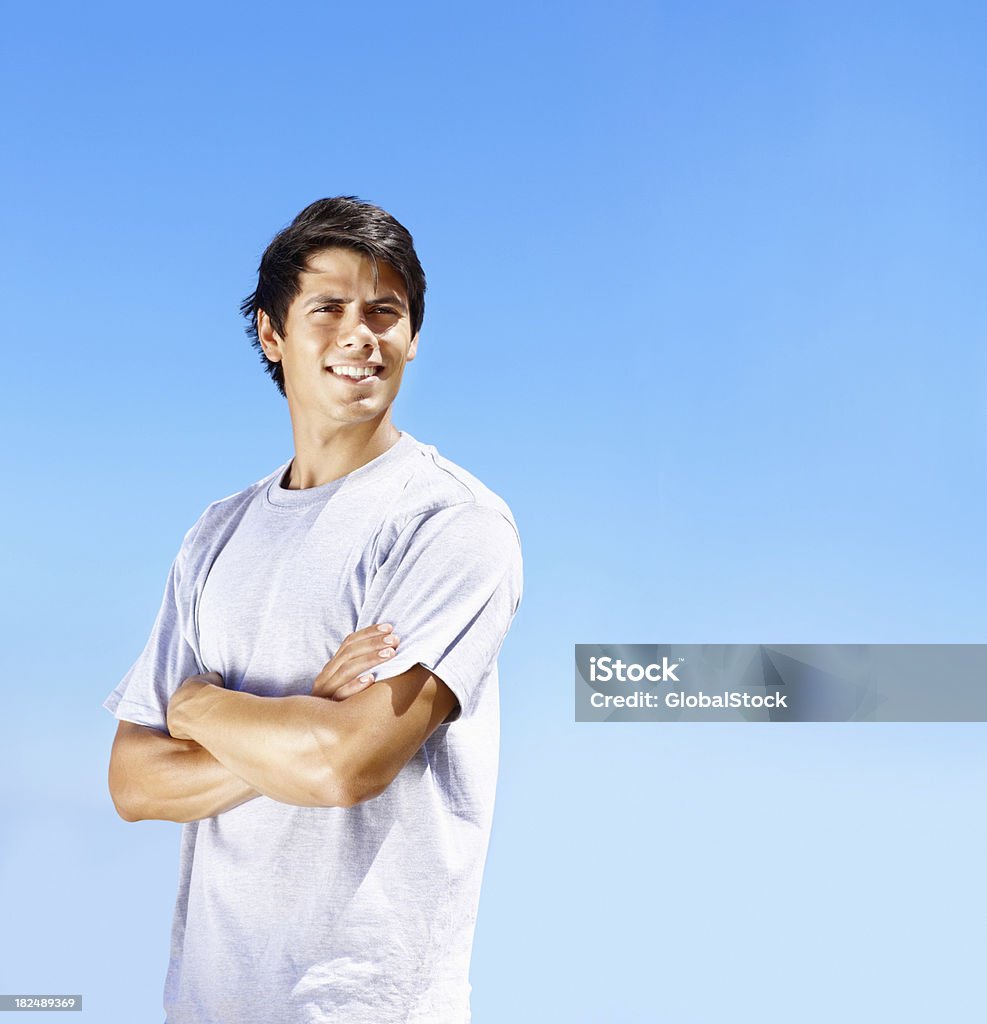 Souriant jeune homme avec bras croisés contre clair ciel - Photo de Jeunes hommes libre de droits