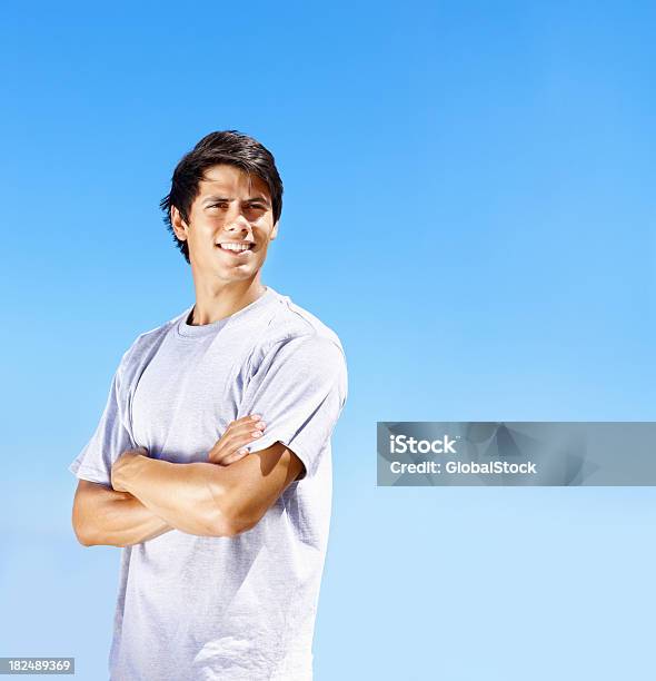 Photo libre de droit de Souriant Jeune Homme Avec Bras Croisés Contre Clair Ciel banque d'images et plus d'images libres de droit de Jeunes hommes