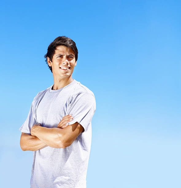 istock Smiling young guy with arms crossed against clear sky 182489369