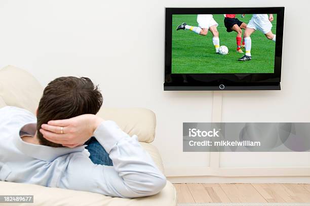 Photo libre de droit de Homme Regarde Un Match De Football À La Télévision À La Maison banque d'images et plus d'images libres de droit de Canapé