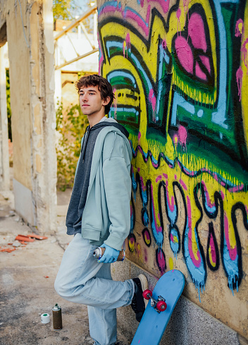 Young man with spray cans standing in front of a graffiti wall