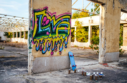 Street artist painting colored graffiti on public space wall - Modern art concept of urban guy performing and preparing live murales paint with yellow aerosol color spray - Cloudy afternoon filter