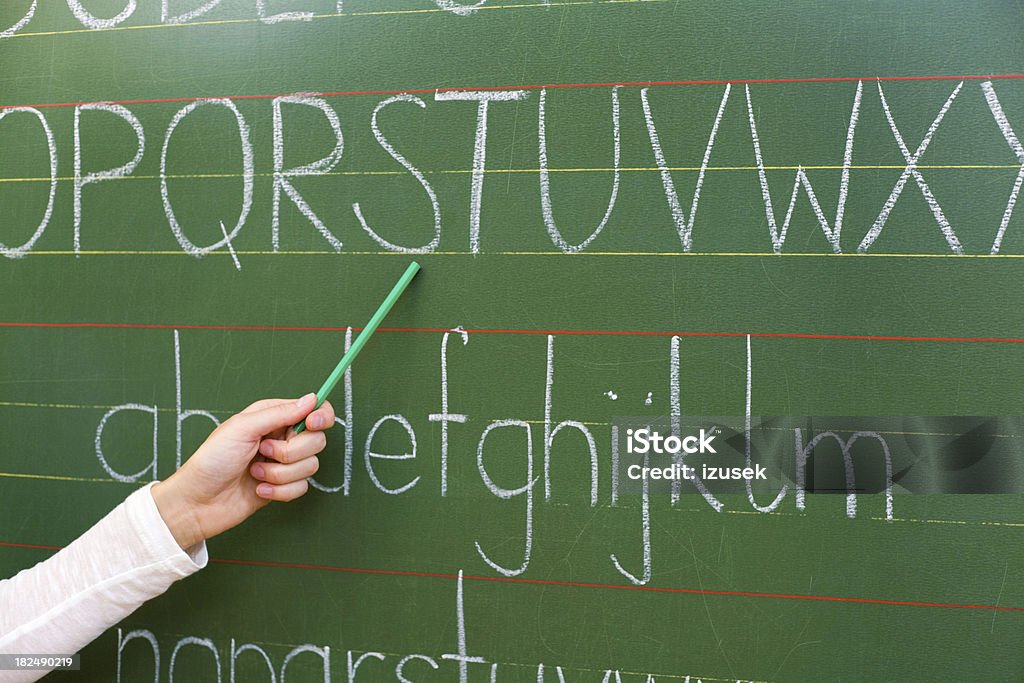 Teaching The Alphabet A teacher's arm pointing at the letters of the alphabet on a blackboard. Adult Stock Photo