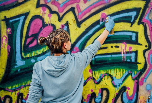 Street artist painting colored graffiti on public space wall - Modern art concept of urban guy performing and preparing live murales paint with yellow aerosol color spray - Cloudy afternoon filter