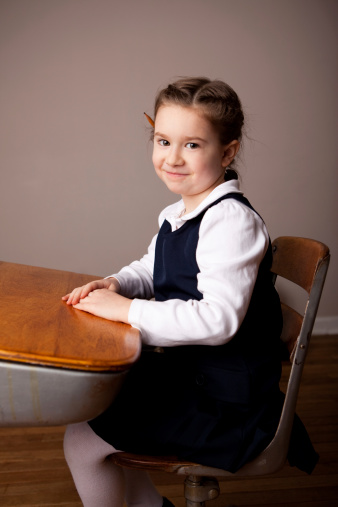 Color photo of a happy six year old girl student smiling while sitting in her school desk.