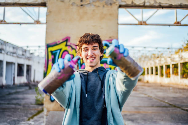 Portrait of young smiling male graffiti artist with spray cans