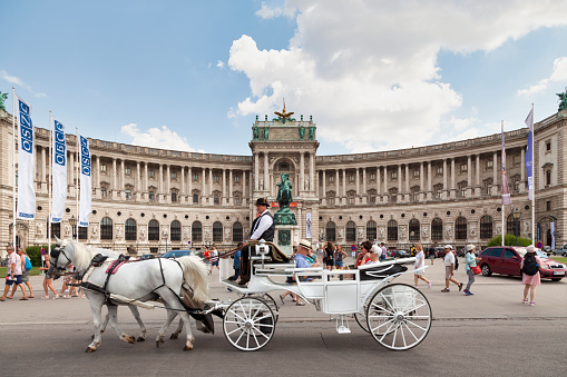 Vienna, Austria - June 17 2018: Carriage passing in front of the Austrian National Library located in the Neue Burg Wing of the Hofburg in center of Vienna.
