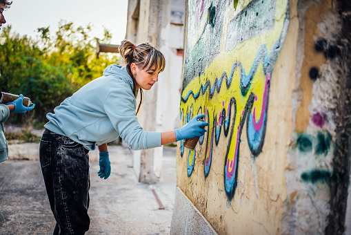 Young female street artist painting colorful graffiti on wall