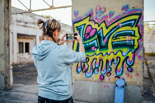 Young woman taking photos of the colorful graffiti on the wall