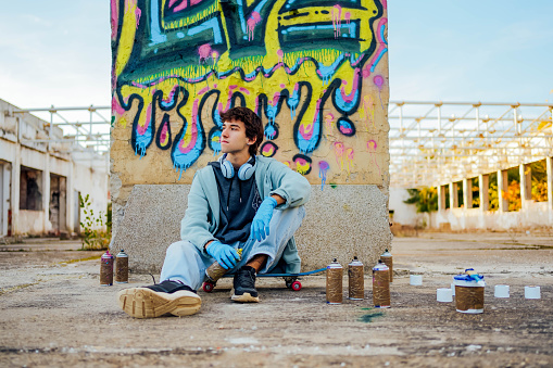 Young man sitting on a skateboard in front of the graffiti on the wall