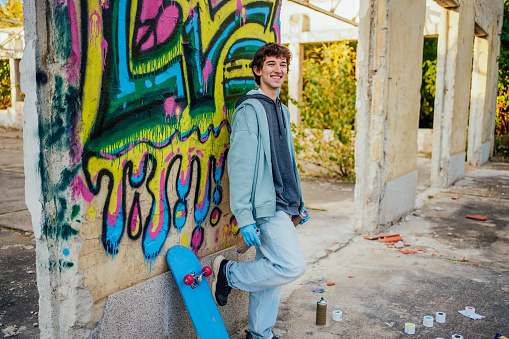 Young smiling man with spray cans standing in front of a graffiti wall