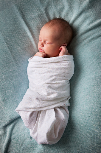 Color photo of a newborn baby sleeping peacefully while wrapped in a blanket.