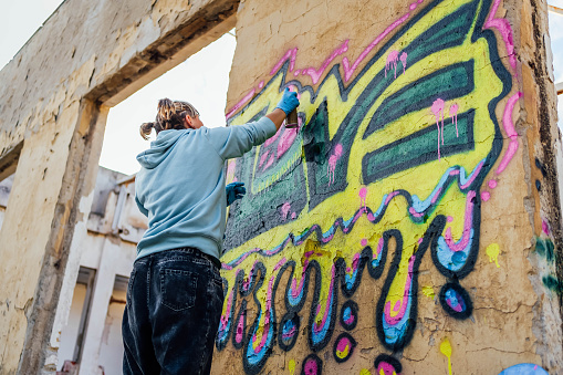 Young female street artist draws graffiti using colorful sprays