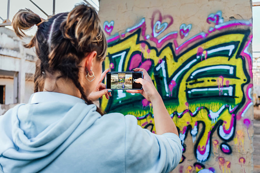 Young woman taking photos of the colorful graffiti on the wall