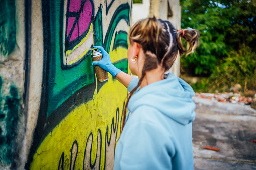 Young woman painting colorful graffiti on a wall