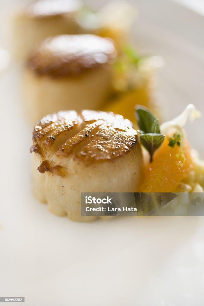Scallops "Very close up, shallow dof shot of 3 seared scallops on a plate with orange sections and mint leaves" Scallop Stock Photo