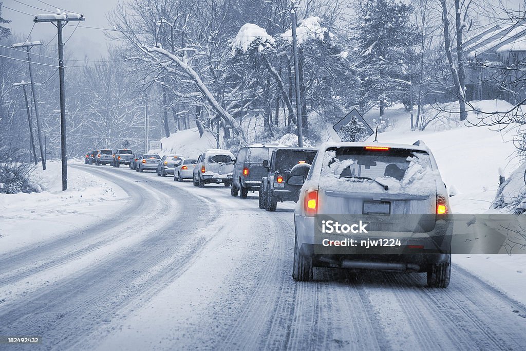 Winter Driving in Snow A line of cars slowly driving on a snowy, icy road. Entire image is monochrome blue-ish except the taillights, which are glowing red and yellow. Winter Stock Photo