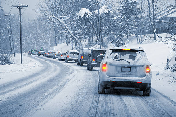 Winter Driving in Snow A line of cars slowly driving on a snowy, icy road. Entire image is monochrome blue-ish except the taillights, which are glowing red and yellow. blizzard stock pictures, royalty-free photos & images