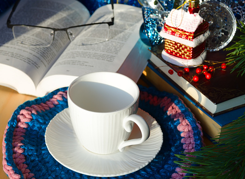 An empty cup for tea or coffee against a background of books and green Christmas tree branches. Decorations for the New Year and Christmas. A place for congratulations.