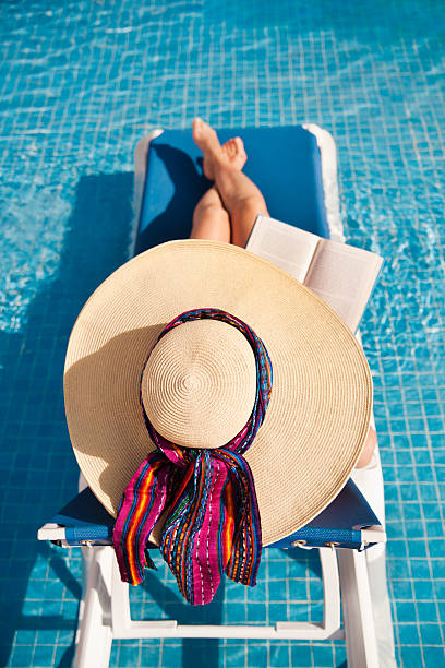 istock Summer Scene—Woman Sunbather Reading in Aqua Blue Swimming Pool 182494453