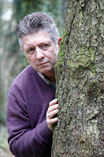 istock Mature man peeking out from woodland tree 182495204