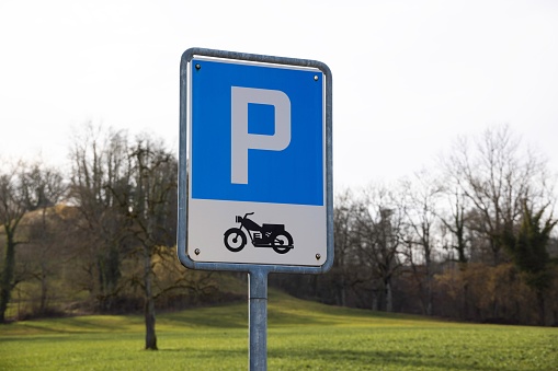 Swiss blue and white parking lot sign for motorcycles, cloudy background forest, daytime without people